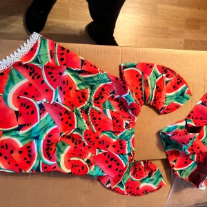 Body klänning med vattenmelonmönster - Supergullig klänning med matchande pannband färgglatt vattenmelonmönster i rött, grönt och svart. Klänningen har puffiga korta ärmar och söt vit spetsdetalj vid fållen. Perfekt för sommarens alla äventyr.  Storlek ca: 1 år +