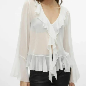 Vit volangblus från Vero Moda - Supersöt vit blus från Vero Moda med volanger längs v-ringningen och nederkanten. Blusen är i ett tunt, lätt och transparent material med långa ärmar som har utsvängda avslut. Helt oanvänd! Nypris 400kr