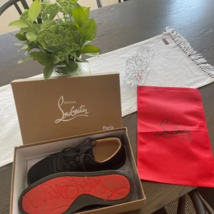 Christian Louboutin svarta sneakers mocka - Snygga svarta sneakers från Christian Louboutin i mocka med klassisk röd sula och svarta skosnören. Skorna har rund tå och platt sula, samt diskreta detaljer som gör dem riktigt stilrena. Perfekta för dig som vill ha något exklusivt och unikt.köpt av en kompis.