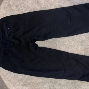 Svarta mjukisbyxor från Nike - Svarta mjukisbyxor från Nike med klassisk vit swoosh-logga på höften. Byxorna har resår i midjan och en bakficka med knapp. Perfekta för chill eller träning, med en skön och avslappnad passform. Står fel på tagen att det är storlek XXL men egentligen äre M/L