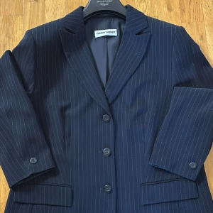 Mörkblå randig kavaj från Gerry Weber - Snygg mörkblå kavaj med tunna vita ränder från Gerry Weber. Klassisk modell med tre knappar framtill, spetsiga slag och fickor med lock. Perfekt för dig som gillar stilrena och tidlösa plagg. Fodrad insida för extra komfort.