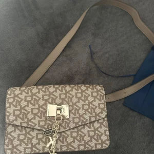 Beige axelväska från DKNY med monogram - Dkny midjeväska. Sista måttet (där man kan reglera måtten, är sliten)