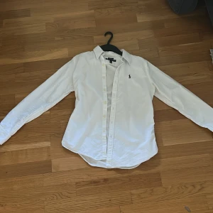 Ralph lauren skjorta - Jätte snygg vit ralph lauren skjorta. Skjortan är slim fit. Knappt andvänd och passar till princip varje outfit. Jätte snygg nu inför sommarn och släpps för ett schysst pris vid snabb affär. Ps: det finns en liten fläck som knappt synns kan säkert tas bort med tvättmedel.