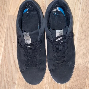 Svarta klassiska sneakers med snörning - Svarta sneakers från Bata med klassisk design och rund tå. Skorna har svart textilöverdel, svarta skosnören och vit sula. Perfekta för en enkel och stilren look. Snygga till jeans eller shorts.