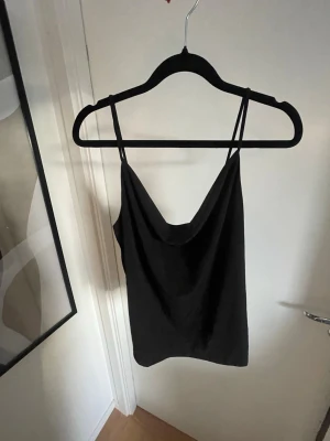 Svart linnetopp med tunna axelband - En svart linnetopp med tunna axelband och snygg draperad ringning. Från BikBok, storlek L