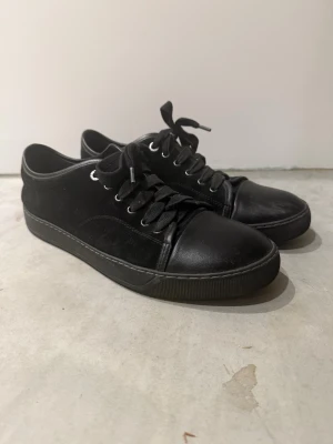 Lanvin - Lanvin sneakers i helsvart med snygg kombination av mocka och skinn. Rund tå, platt sula och klassisk snörning med metallöglor. Stilren design som passar till många olika looks. Kommer med originalkartong.