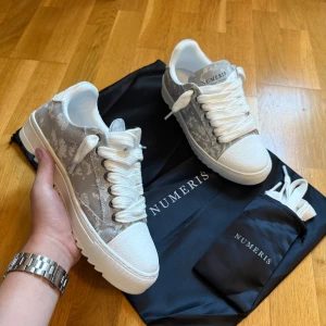 Numeris ”Visual Thinking” - Snygga sneakers från Numeris i grått och vitt med subtilt blommigt mönster. Skorna har breda vita snören, vit platt sula med räfflad undersida och detaljer i både textil och skinn