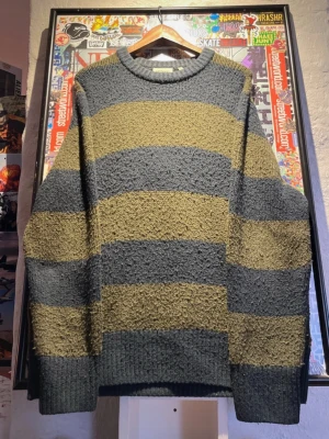 Randig stickad tröja från Carhartt - Säljer en grovstickad tröja från Carhartt i mörkgrått och olivgrönt med breda ränder. Tröjan har rund halsringning, lång ärm och en loose fit. Perfekt för dig som gillar streetwear och vill ha en chill vibe.