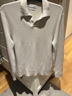 Beige merinoull pikétröja These Glory Days - Säljer en stilren beige pikétröja från These Glory Days i Superior Merinoull. Tröjan har lång ärm, klassisk krage och diskret struktur i tyget som ger en exklusiv känsla. Perfekt för dig som gillar en clean och tidlös look.