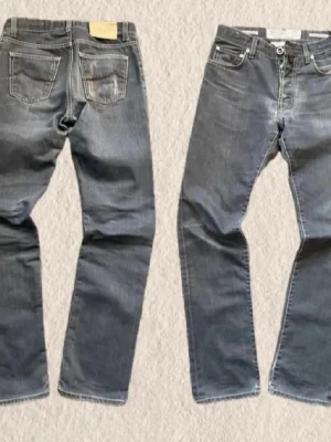 Grå jeans från Jacob Cohen - Snygga grå jeans från Jacob Cohen med klassisk femficksdesign och kontrastsömmar. Jeansen har raka ben och en ljus tvätt som ger en avslappnad look. Tillverkade i slitstarkt bomullsmaterial med Jacob Cohen-läderpatch bak i midjan. Väldigt bra skick| hör av er minsta lilla| Mått midja 38 runt 84 innerbenet