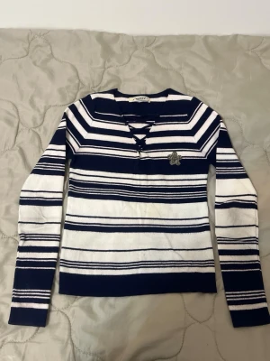 Randig stickad tröja från Queen's - Säljer en marinblå och vit randig stickad tröja från Queen's. Tröjan har lång ärm, snörning vid halsen och en glittrig stjärndetalj på bröstet. Perfekt för dig som gillar en chill men ändå snygg look.
