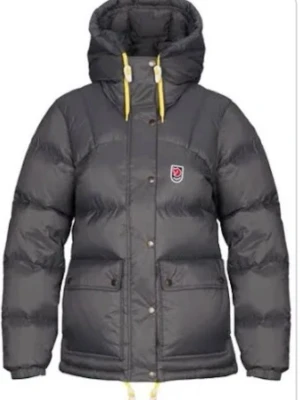 Grå dunjacka från Fjällräven xxs  - Vinterjacka från Fjällräven med gul snörning i huvan och klassisk logga på bröstet. Jackan har stora fickor framtill, tryckknappar och dragkedja. Perfekt för kalla dagar med sin tjocka vaddering och justerbar huva.   strl xxs. Jackan är i nyskick och har inga defekter. Inköpt på naturkompaniet för 7499kr 