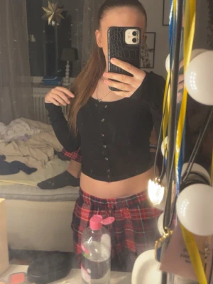 Svart ribbad croppad topp med knappar - Säljer en svart croppad topp med långa ärmar och ribbad struktur. Toppen har en snygg knappdetalj framtill och sitter tight mot kroppen. Perfekt att styla med jeans eller kjol för en trendig look.