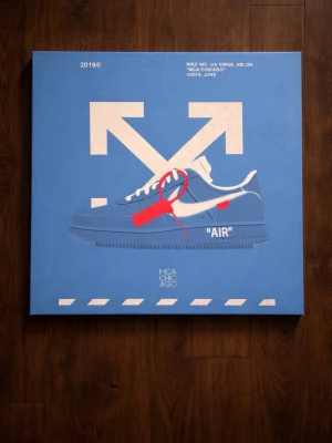 Blå poster Off-White x Nike Air Force 1 - Poster med motiv av Off-White x Nike Air Force 1 'MCA' i blått med vit swoosh och röd tag. Stor vit Off-White-pil i bakgrunden och textdetaljer som 'MCA CHICAGO' och '2019, JUNE'. Perfekt för sneakerheads och streetwear-fans.