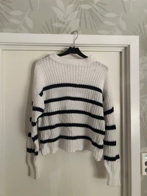 Vit stickad randig tröja - Säljer en vit stickad tröja med svarta ränder. Tröjan har en ribbad struktur och lång ärm. Säljer för att den inte kommer till användning längre. 