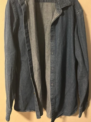 Mörkblå jeansskjorta från Massimo Dutti  - Säljer en klassisk mörkblå jeansskjorta i bomull med långa ärmar och knappar framtill. Skjortan har en avslappnad passform och tidlös look, perfekt att styla lager på lager. Inga synliga loggor eller märken. Från Massimo Dutti.