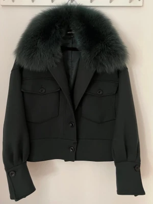 Mörkgrön jacka med fuskpäls från Meotine - Snygg mörkgrön jacka från Meotine med stor, fluffig fuskpäls i kragen i storlek S/M. Säljer pågrund av att den inte kommit till användning super fin jacka som jag använt ca 2 gånger. Skriv för mer bilder eller info!😊🥰