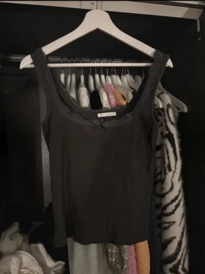 Svart linnetopp med spetskant - Säljer en svart linnetopp med breda axelband och dekorativ spetskant runt urringningen. 