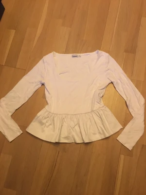 Vit volangblus från Stradivarius - Supersöt vit blus från Stradivarius med lång ärm och volang nertill. Blusen har en rundad, djupare ringning och är tillverkad i mjuk material ,volangen är gjord av bomull . Perfekt att styla med jeans eller kjol för en fräsch look.