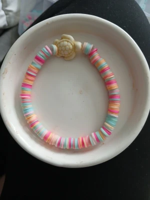 Pastellfärgat armband med sköldpadda - Ett armband med platta pärlor i pastellfärger som rosa, blå, vit och orange. Armbandet har en söt pärla formad som en sköldpadda i mitten. Perfekt accessoar för dig som gillar färg och unika detaljer.
