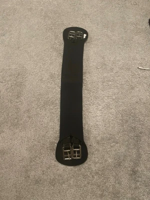 Svart ridgjord 70 cm - Säljer en svart ridgjord i syntetmaterial, 70 cm lång. Den har dubbla metallspännen i båda ändar för enkel fastsättning på sadeln. Perfekt till ridning och passar till de flesta sadlar. Kommer tyvärr inte ihåg vilket märke de är för den är köpt i ullared. Har bara testat den men den var för liten så den har bara används en gång. Tror jag köpte den för ungefär 100 kr.