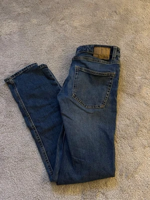 Blå slim jeans  - Säljer ett par klassiska blå slim fit jeans från lager 157 i storlek W28 L32. Jeansen har en snygg mörkblå tvätt, raka bakfickor och diskreta sömmar. Perfekta för dig som gillar en smalare passform och tidlös stil.