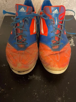 Adalidas Adizero leather blå/röda fotbollsskor - Säljer ett par Adidas Adizero fotbollsskor i blått och rött med vita detaljer. Skorna har klassisk snörning, låg profil och tre vita ränder på sidan. Ovandelen är i syntetmaterial och designen är sportig och lätt för snabba rörelser på planen.                                Pris kan diskuteras!!
