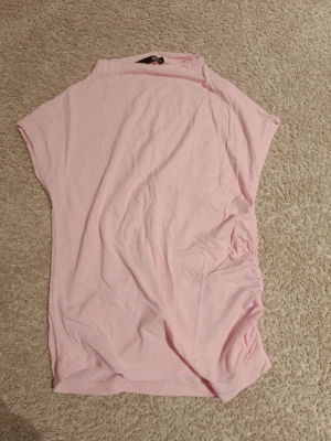 Top med dragsko - Rosa top med inga ärmar och lite högre hals. Dragsko på ena sidan. Storlek s från lager
