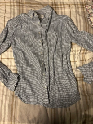 Rutig skjorta från The Shirt Factory - Säljer en slim fit skjorta från The Shirt Factory i vitt och blått rutigt mönster. Skjortan har klassisk krage, långa ärmar och knäppning framtill. Perfekt för dig som gillar stilrena och tidlösa plagg.