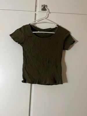 Olivgrön ribbad topp Pull&Bear - Säljer en olivgrön ribbad topp från Pull&Bear i storlek M. Toppen har korta ärmar, rund halsringning och är tillverkad i ett mjukt, stretchigt material. Perfekt till jeans eller kjol för en enkel och snygg look.