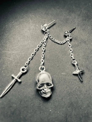 By prisförslag- 1 st dubbel Silvrig kedjeörhänge med svärd döskalle  och stjärna - Unikt örhänge i silverfärgad metall med kedjor och tre hängen: ett svärd, en dödskalle och en stjärna. Kedjorna kopplar ihop två öronstift för en edgy och cool look. Perfekt accessoar för dig som gillar detaljer med attityd.