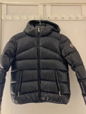 Svart pufferjacka från Colmar - Säljer en svart pufferjacka från Colmar med huva och två dragkedjeförsedda fickor. Jackan har en glansig finish och tydliga quiltade partier. Perfekt för dig som vill ha en varm och snygg jacka till vintern. Strl 12 years men sitter mer som en xs på mig. Skulle säga att de är större i storleken. Tveka inte att höra av er eller något!