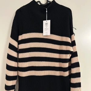 Randig stickad tröja från VILA - Snygg randig stickad tröja i svart och beige från VILA i storlek XS. Tröjan är i längre modell och har långa ärmar och en ribbad design med slits på båda sidorna. Aldrig använd och har prislappen kvar. Köptes för 499 kr.