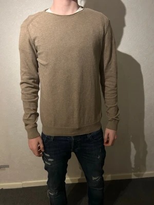 Beige stickad tröja från Indicode - Snygg beige stickad tröja från Indicode i storlek small. Tröjan har rund halsringning och långa ärmar med ribbade muddar. Modellen är 183