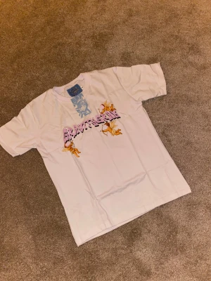 Vit Gravity Grab t-shirt med änglar - Vit t-shirt från Gravity Grab med tryck i lila och svart text samt söta änglar på bröstet. Klassisk passform och rund halsringning. Perfekt för dig som gillar streetwear och coola prints. Limted edition!