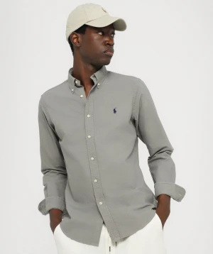 Grå skjorta från Ralph Lauren - Snygg grå skjorta från Ralph Lauren med klassisk button-down krage och mörkblå broderad logga på bröstet. Slim fit-modell i mjuk bomull, med vita knappar och lång ärm. Perfekt för dig som gillar stilrena och tidlösa plagg.