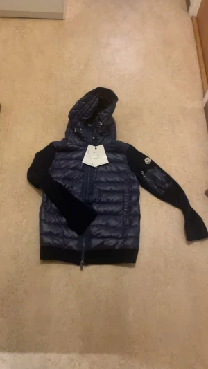 Moncler cardigan - Snygg marinblå pufferjacka från Moncler med huva och dragkedja framtill. Jackan har quiltad framsida och rygg i glansigt material, samt svarta stickade ärmar med Moncler-logga på vänster arm. Perfekt för kyliga dagar. Det är S men passar även som M. Skriv om du har frågor!! Pris kan diskuteras vid snabb affär!!!