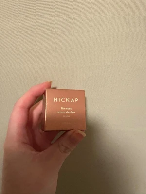 Hickap Fire Eyes Cream Shadow Stardust - Fire Eyes Cream Shadow från Hickap i nyansen Stardust är en krämig ögonskugga med metallisk finish. Färgen är en skimrande roséguld-brons som ger ögat ett glansigt och intensivt uttryck. Kommer i en rund burk med ljus lock och guldtext. Perfekt för dig som gillar glow och pigment.