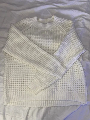 Vit stickad tröja med grov struktur - Säljer en vit stickad tröja med grov, strukturerad stickning och breda ribbade muddar vid ärmslut och nederkant. Tröjan har rund halsringning och lång ärm, perfekt för lager på lager under kyliga dagar.