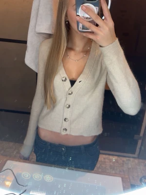 Beige croppad kofta med knappar - Superfin beige croppad kofta från Zara med v-ringning och snygga knappar framtill. Mjuk stickad känsla och långa ärmar, perfekt att slänga över ett linne eller topp. Enkel och stilren design som är lätt att matcha med jeans eller kjol. Stl S, i nytt skick ❤️kom gärna med prisförslag!