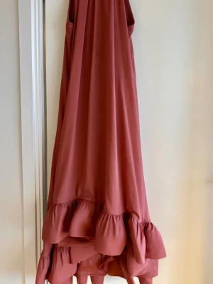 By Malina halterneck klänning XS - Midiklänning från Malina i terracotta. Använd endast två gånger. Halterneck, knyts i nacken, öppen rygg och vid kjol med volangkant. Dold dragkedja baktill. Kemtvätt vid behov.
