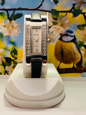 Festlig Damklocka från Zone - Säljer en elegant damklocka från Zone. Klockan har ett quartz urverk och en rektangulär urtavla med dekorativa stenar runt om. Armbandet är tillverkat av läder.Nyskick med plast på fram/ baksida samt nytt batteri.