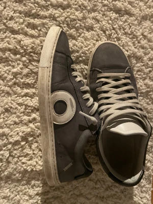 Oliver Cabell grå sneakers - Snygga grå sneakers från Oliver Cabell med vit sula och vita snören. Skorna har en rund tå och är tillverkade i skinn/mocha med en unik vit cirkeldetalj på sidan. Perfekta för dig som gillar stilrena och moderna sneakers. Skriv om du har frågor, priset kan diskuteras!