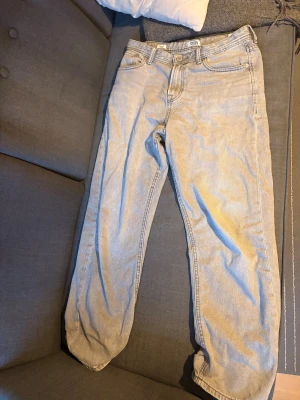 Ljusgrå jeans från Jack & Jones - Säljer ett par ljusgrå jeans från Jack & Jones i storlek 158. Klassisk femficksmodell med raka ben och snygga sömdetaljer på bakfickorna. Jeansen är tillverkade i bomull och har en stilren look som passar till det mesta.