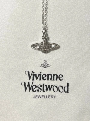 Vivienne Westwood silver halsband - Säljer ett ikoniskt Vivienne Westwood halsband i silverfärgad metall med den klassiska orb-berlocken dekorerad med små glittrande stenar. Kedjan är tunn och elegant, perfekt för att ge din outfit en edgy touch. Levereras med originalpåse och putsduk. Ett till ett!!!