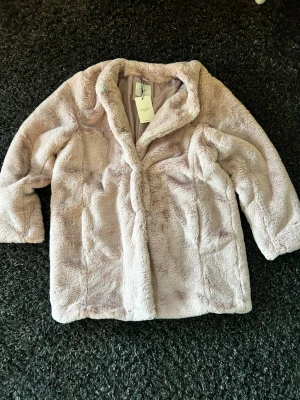Ljusrosa pälsjacka från Cellbes - Säljer en fluffig och mjuk ljusrosa pälsjacka från Celebs. Jackan har en klassisk krage och raka ärmar, perfekt för dig som vill ha en cozy vibe. Fodrad insida och enkel design gör den lätt att matcha med din stil.