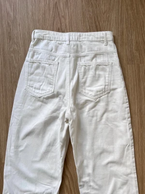 Cremevita jeans från NA-KD  - Snygga vita jeans från NA-KD i storlek 36. Högmidjade med raka ben och har slitsdetaljer vid bensluten. Använda ett par gånger för några år sedan. Önskar du veta exakta mått? Tveka inte att höra av dig!