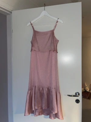 Glittrig rosa långklänning Soaked - Säljer en glittrig rosa långklänning från Soaked in Luxury i storlek XS. Klänningen har smala axelband, volangdetalj upptill och en bred volang längst ner. Materialet är skimrande och känns lyxigt, perfekt för dig som vill sticka ut med en feminin look.