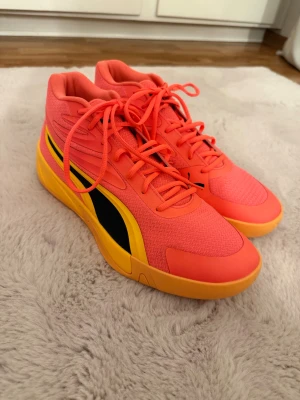 Puma Träningsskor  - Snygga tränings skor från Puma i en cool orange/rosa färg med gula detaljer och svarta loggor. Skorna har snörning, platt sula och en rund tå. Modellen heter Puma Court Pro i storlek 45, Sparsamt använda, Liten svart fläck på skor där bak, Kan gå ner i pris vid snabb och smidig affär :) 