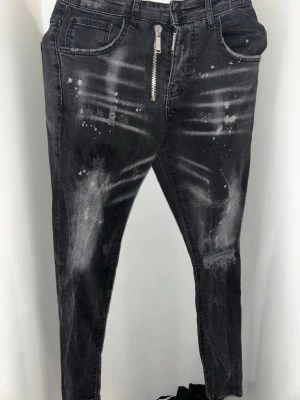 Svarta Dsquared2 skinny jeans med dragkedja - Passar 31/32 bäst. Snygga svarta skinny jeans från Dsquared2 med slitna detaljer, vit färgstänk och en cool dragkedja framtill. Jeansen har en patch med Dsquared2-logga bak och är tillverkade i stretchig denim för en tight passform.